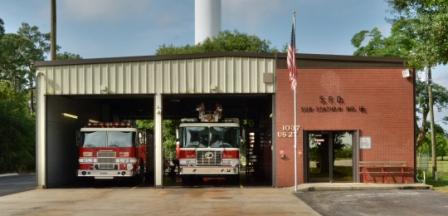Station 15 on Hwy 27, bay doors open with 2 fire trucks inside, american flag on flag pole